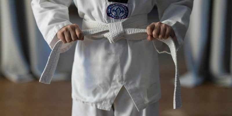 Close-up of a karate student tying a white belt in a traditional martial arts uniform.